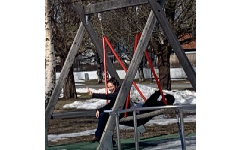 Two adults on a large swing with snow and tress in the background