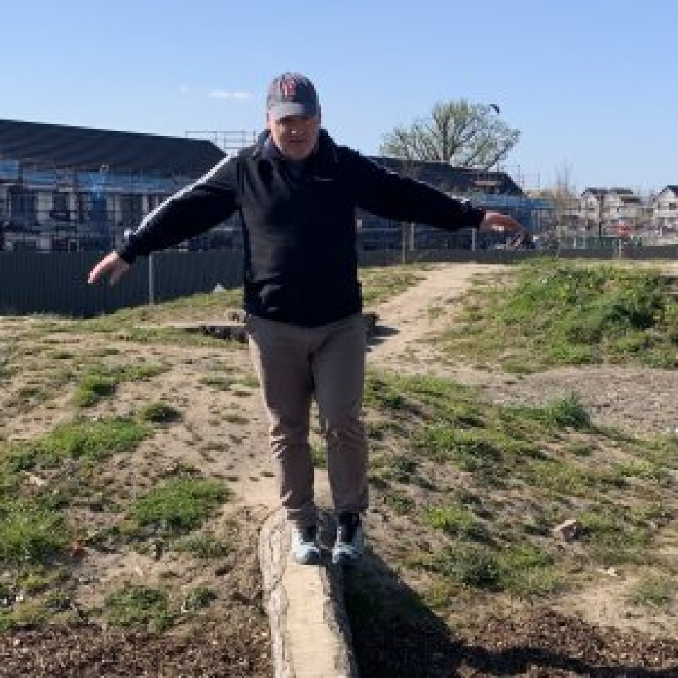 Older man balancing on wooden beam outside