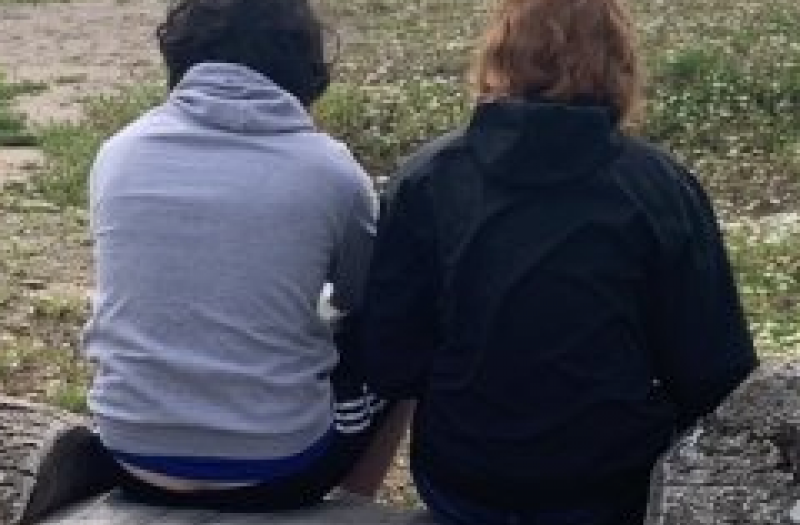 The backs of two people sitting on a stone plnth
