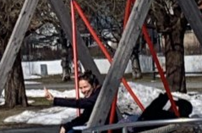 Two adults on a large swing with snow and tress in the background