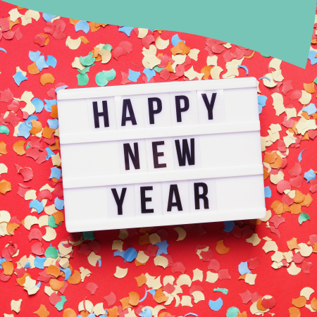 Happy New Year text against a white background, in front of a red surface covered with colorful confetti.