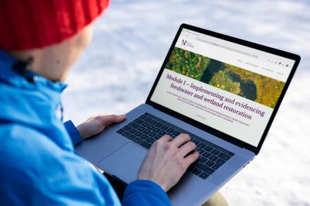 MERLIN academy website mock up on a laptop screen held by a person outside in winter