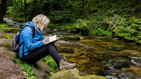 person sat writing in a book by the river