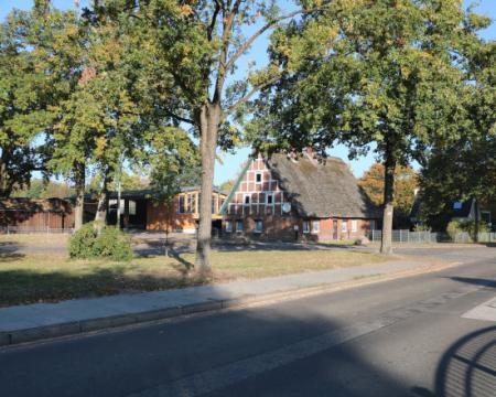 A tree lined street in Hamburg with a historic, vernacular building set back from the road.