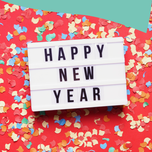 Happy New Year text against a white background, in front of a red surface covered with colorful confetti.
