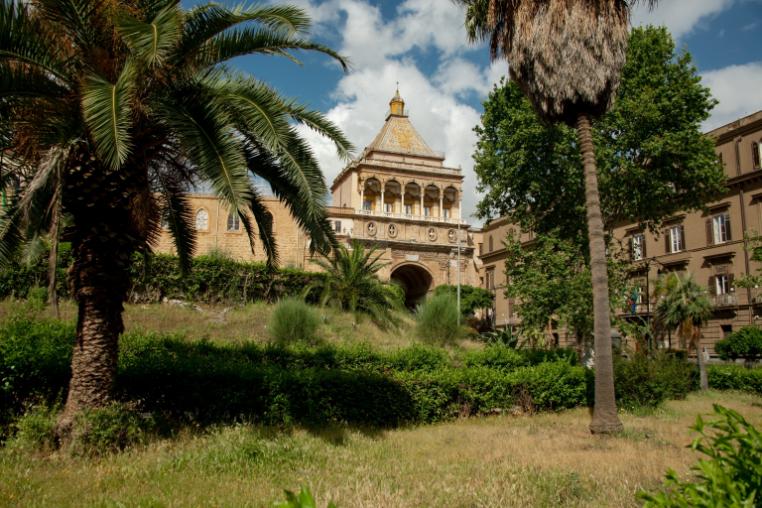 An old building in Palmero with palm trees and grass in front of it.
