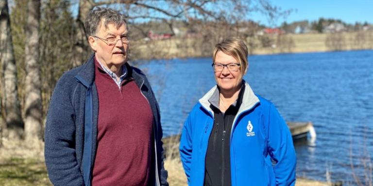 Two people smiling with a water body behind them.
