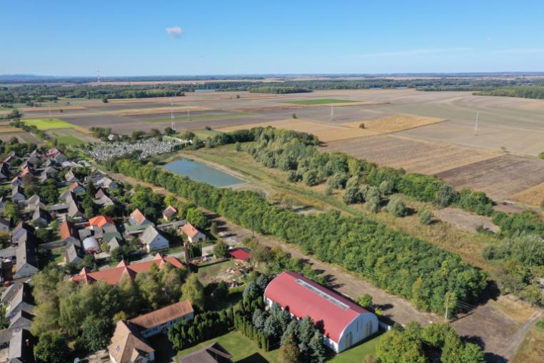 Elevated view of the edge of a settlement next to a large water catchment pond and large, rectangular fields.