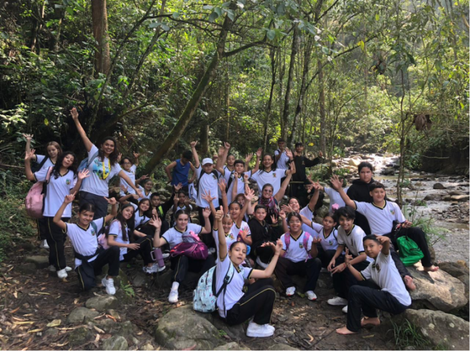 A large group of young people waving their arms and smiling next to a river. 