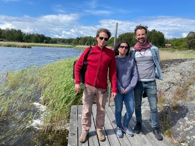 Three people stood on a wooden jetty by the side of a lake.