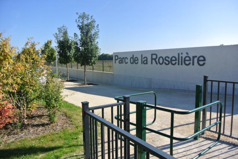 Entrance to a park with tree planting on one side of the path and a sign for the park on the other side of the path.
