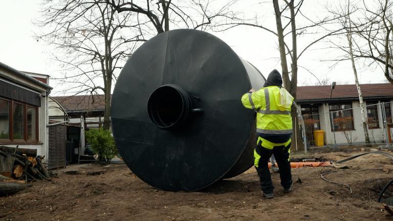 A construction worker moving a large water collection container within the grounds of a kindergarten.